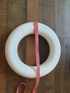 A photo of a polystyrene wreath showing the circumference of the wreath body being measured with a tape measure