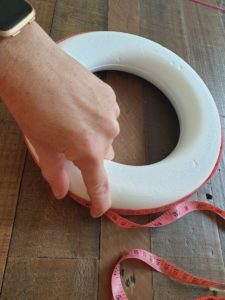 A photo of a polystyrene wreath showing the outer circumference being measured