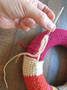 A photo showing the loose ends of yarn threaded onto a needle and being inserted under the crochet piece to hide them
