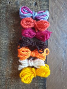 A photo of seven small yarn bundles to show the colours used in the project which were yellow, cream, orange, dark brown, maroon, burnt orange and a mixed pink and blue variegated yarn