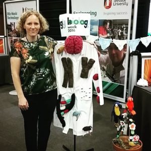 A photo showing Dr Helen Carney standing next to a stand of knitting at the 2016 biology week open day