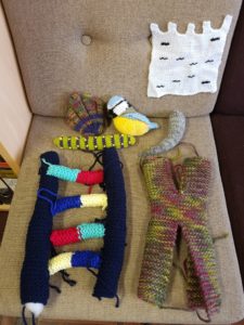 A photo showing knitted items on a chair, showing a knitted blue tit, knitted caterpilar, knitted shell, knitted DNA and chromosome, knitted agarose gel