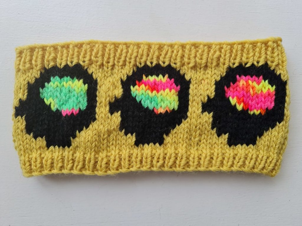 A knitted yellow readback with a pattern that depicts three head silhouettes with different coloured brains.