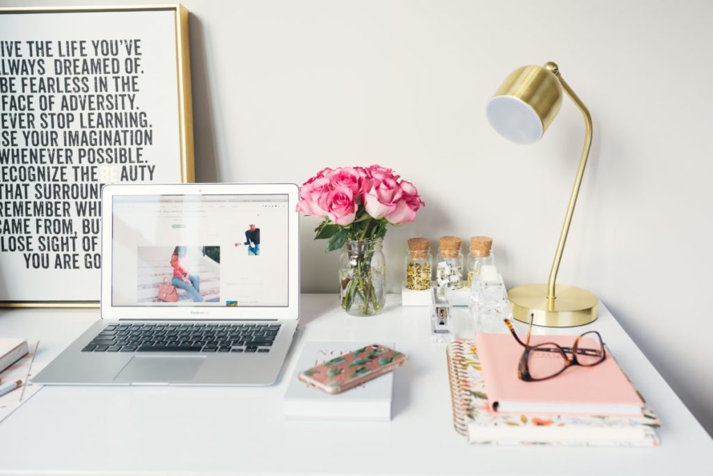 Image of a tidy desk with laptop, desk lamp, notebook and flowers.