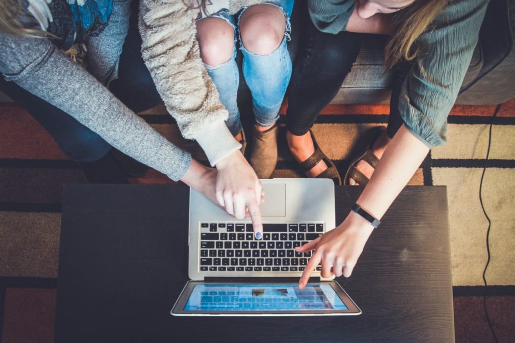 Image shows three friends sitting together and looking at a laptop.