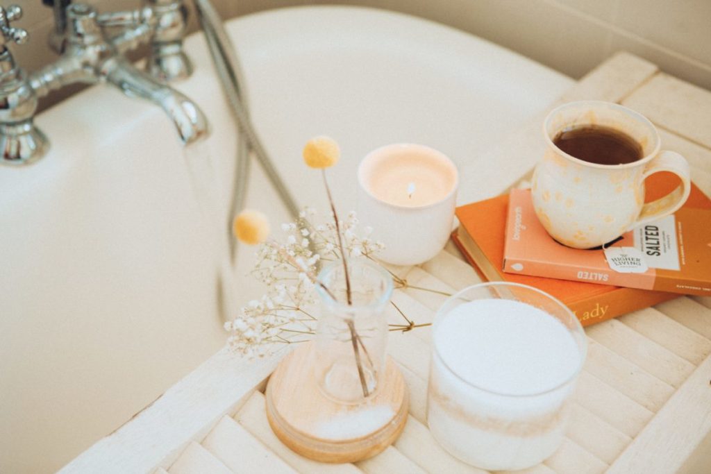 Image of a bath and bath tray, with a book, herbal tea and flowers.