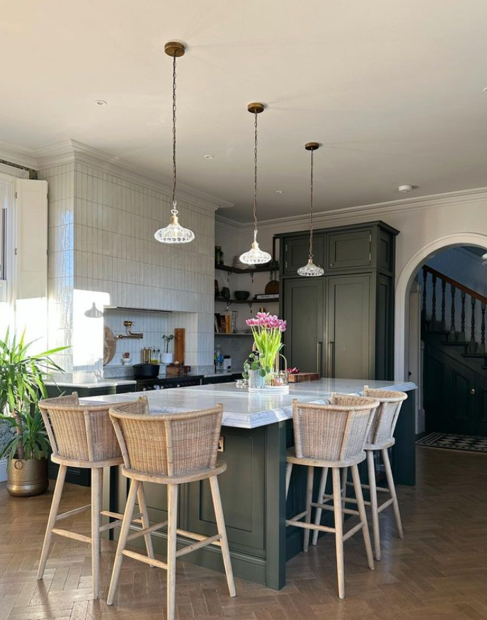 Image shows Rachael's kitchen with two-tone units, woven bar stools and glass pendant lighting.