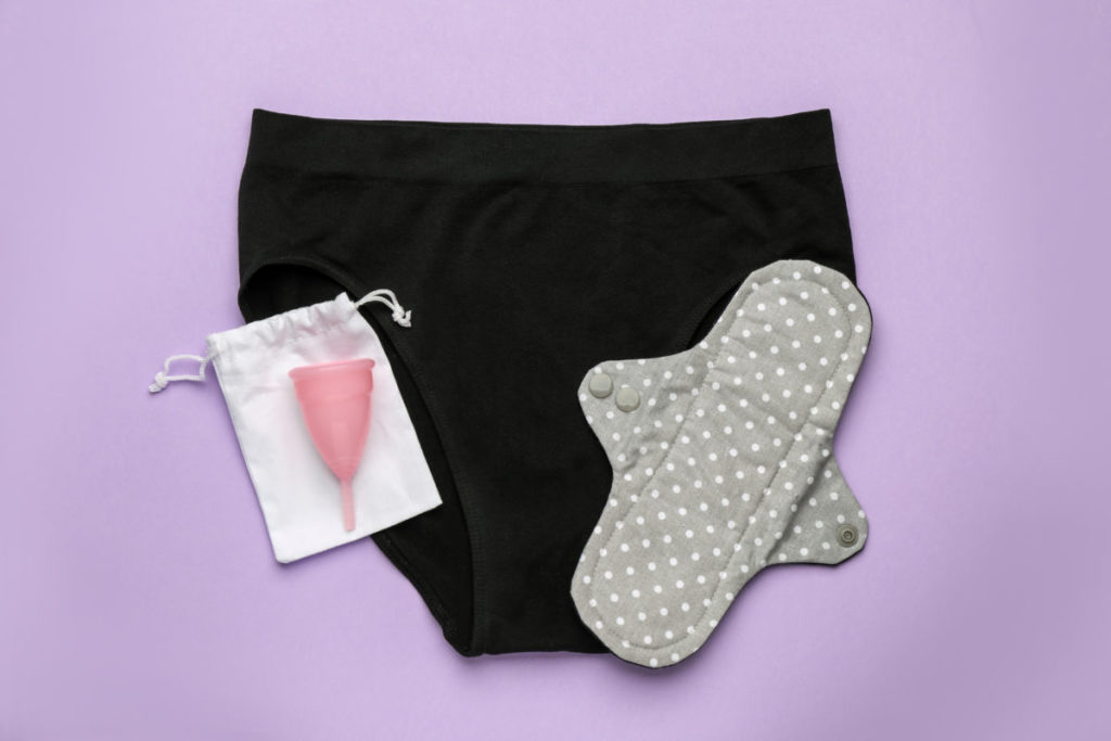 Women's underwear, reusable cloth pad and menstrual cup on violet background