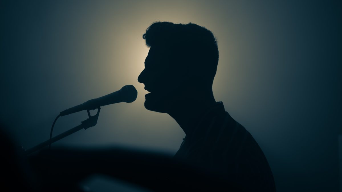 A person singing into a microphone silhouetted against the stage lights