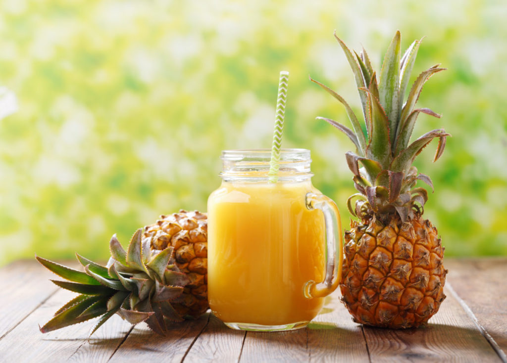 glass jar of pineapple juice with fresh fruits on wooden table