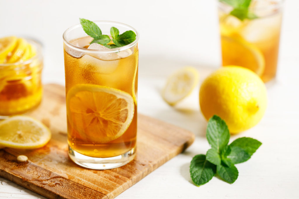 ice tea with sliced lemon and mint leaves in a glass on white wooden table background.