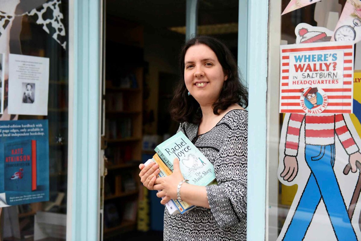 Jenna Warren standing in the doorway of Book Corner, holding a book.
