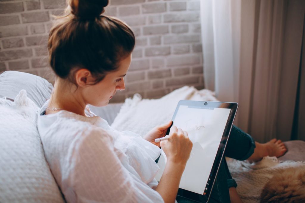 Image shows a young woman making notes on her tablet.