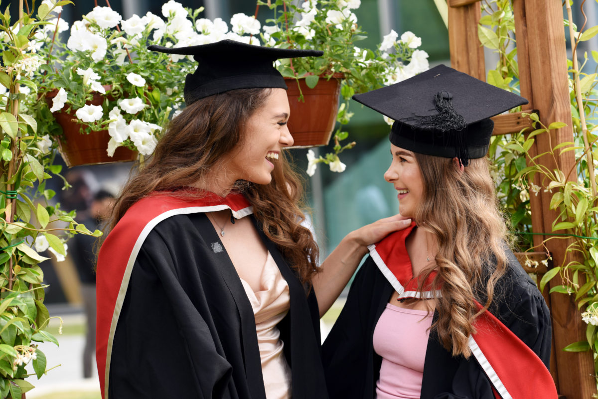 Two graduates smiling under the flower arches