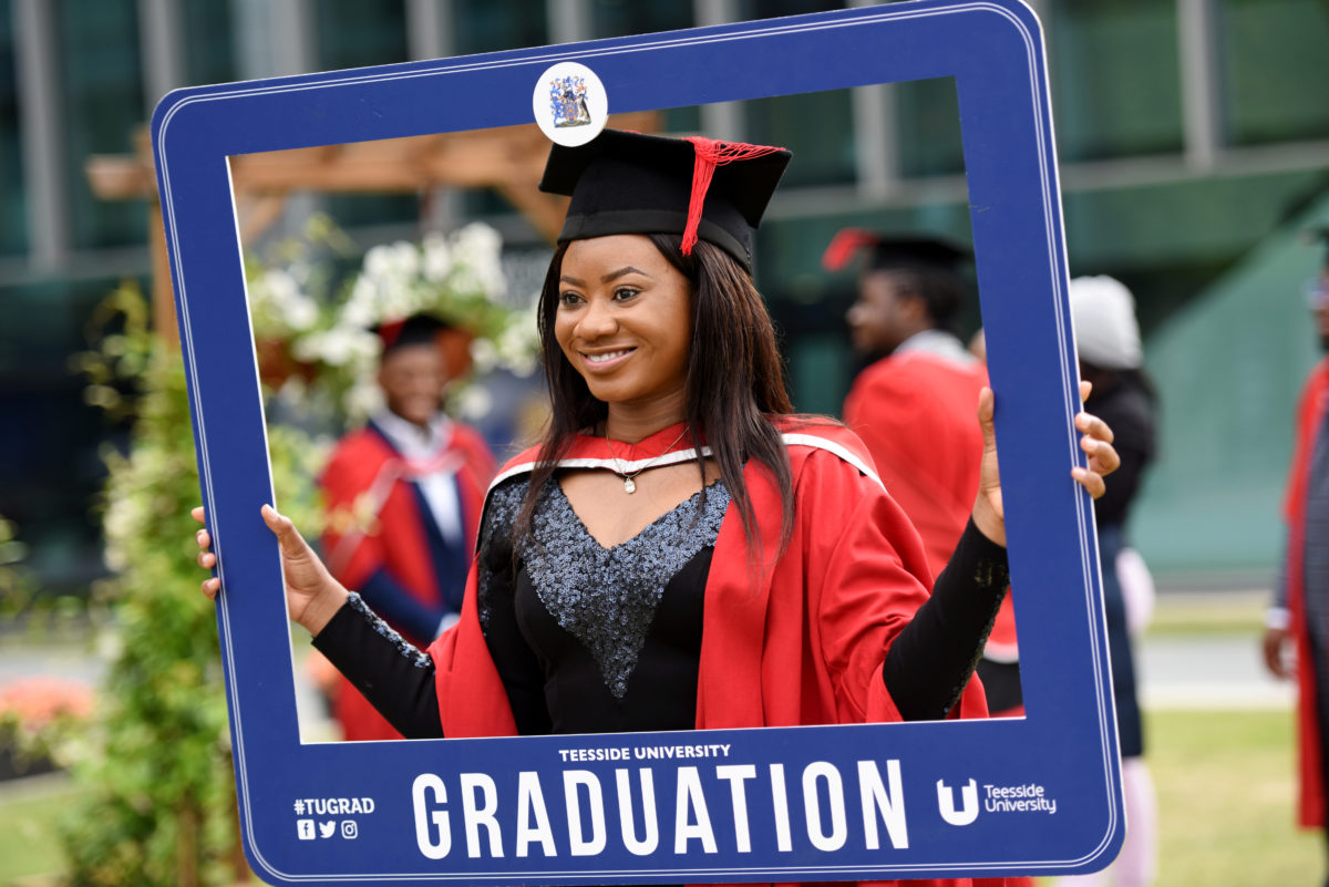 Master's graduate posing in a red gown and holding a blue Graduation prop frame