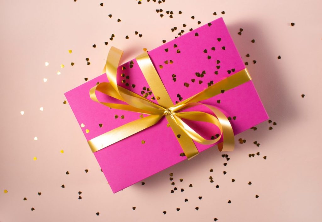 Gift box wrapped in hot pink paper with a gold ribbon and glitter confetti.