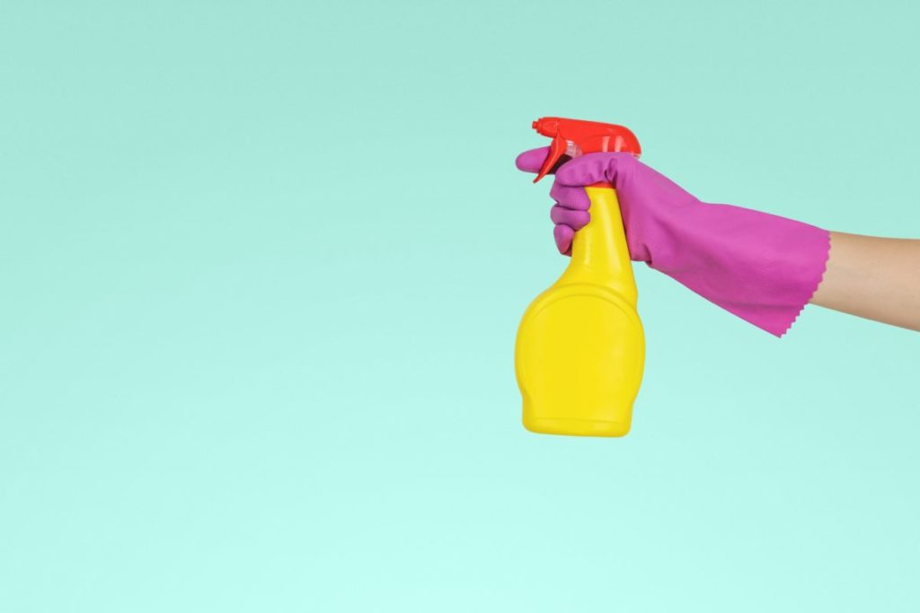 Person holding a cleaning spray against a blue background.