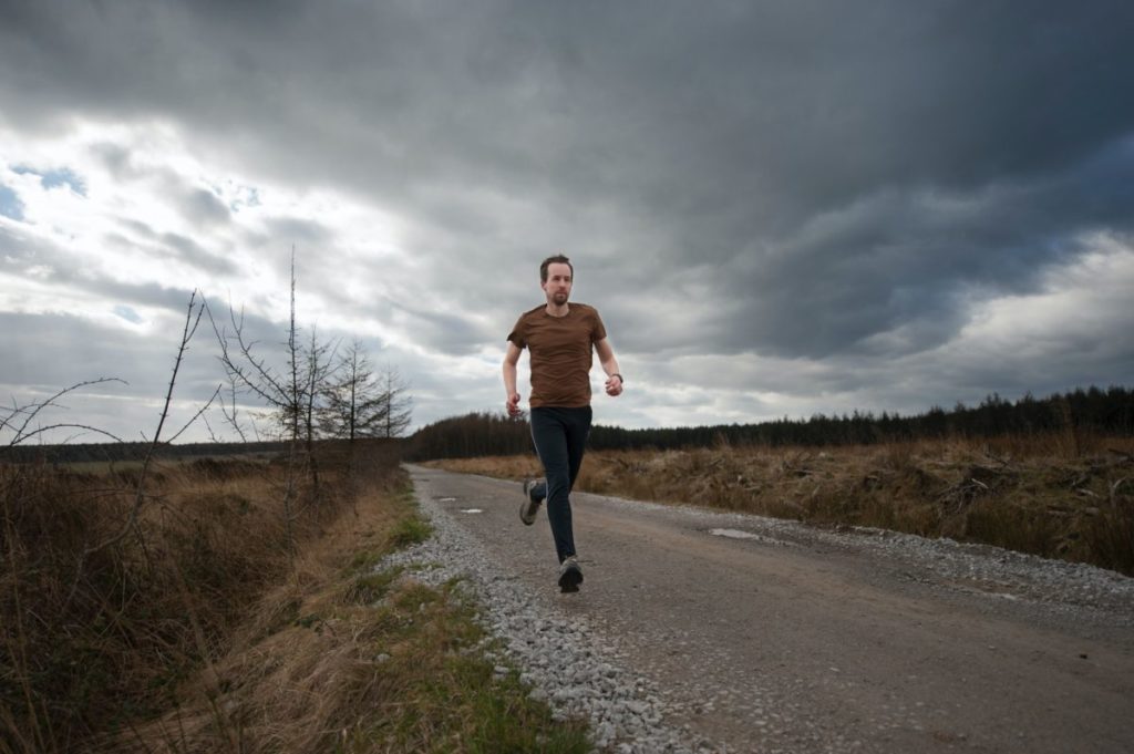 A man running down a country road on a cloudy, wintery day.