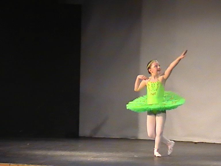 Nikita in a green tutu performing in a dance competition as a child