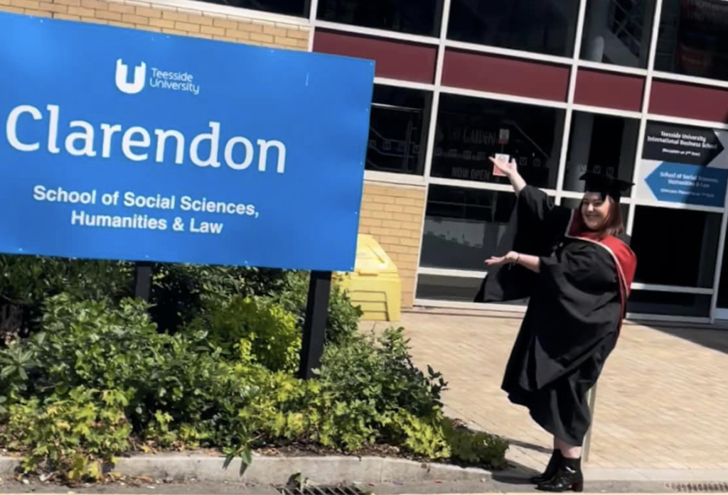 Nikita in black and red graduation robes posing next to a university building