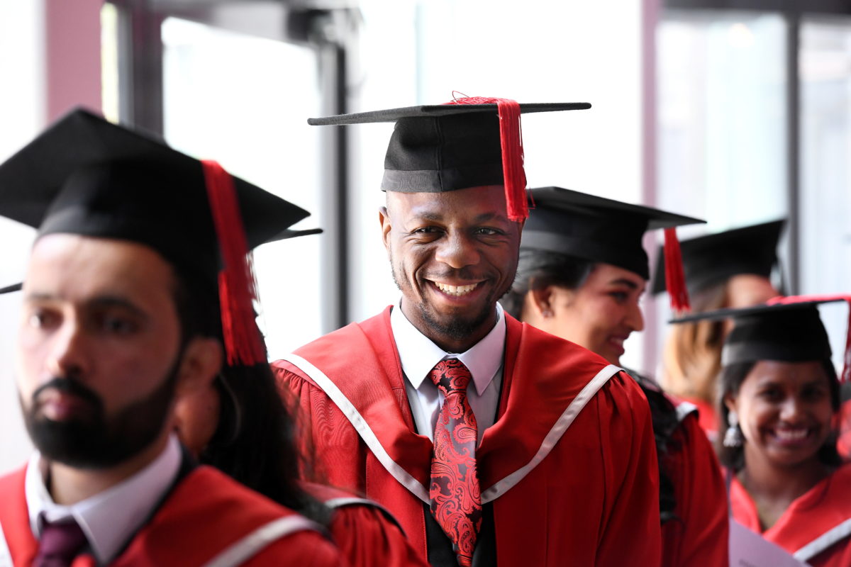 A student wearing red academic robes and a black mortar board about to cross the stage at Graduation
